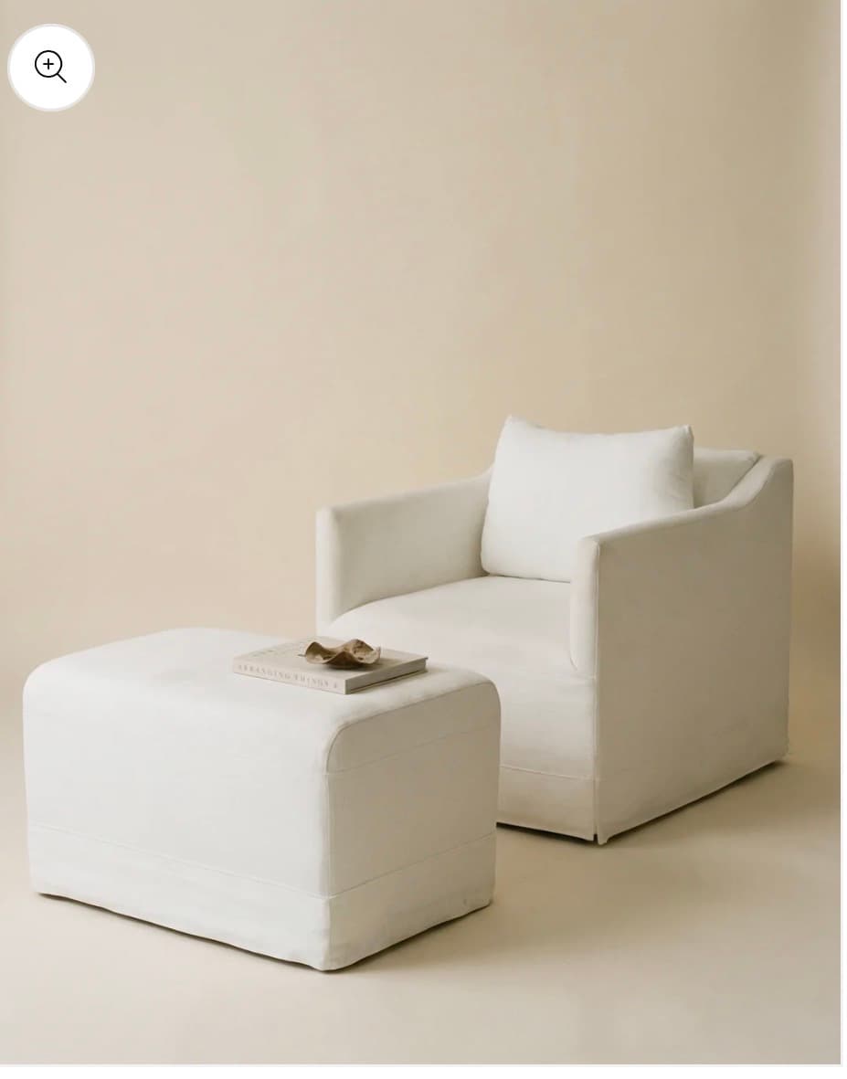 A contemporary upholstered armchair with a matching rectangular ottoman, both featuring removable slipcovers in a light, neutral fabric. — 3D model