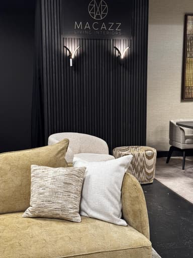 A sectional sofa with a textured, mustard-yellow fabric upholstery. The sofa features a low profile and deep seating. It is adorned with several throw pillows, including one in a neutral tone and others with subtle striped and textured patterns. The base of the sofa has a distinctive geometric pattern. Two dark wood coffee tables with rounded edges are positioned in front of the sofa, and a plush, light-colored rug covers the floor. — 3D model