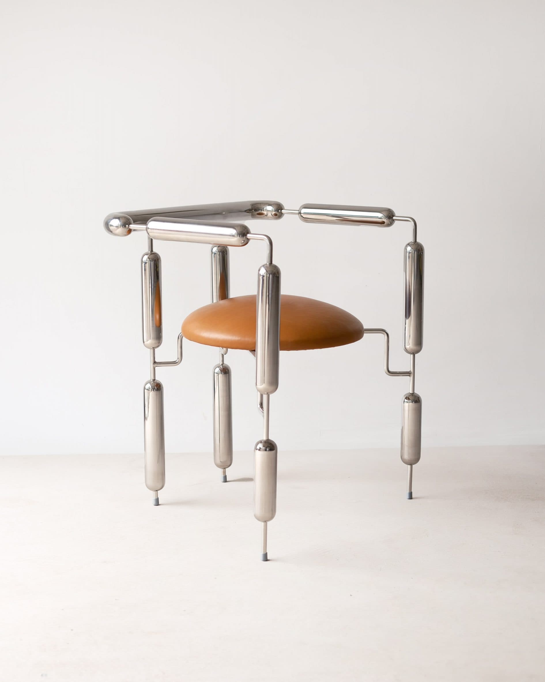 A striking postmodern accent chair featuring a highly polished tubular chrome frame and a circular, tan upholstered seat. The frame is constructed from segmented chrome tubes connected by smaller rods and spherical joints, creating a unique, sculptural silhouette. The design is minimalist yet highly stylized, resembling an avant-garde artistic creation with functional seating. The seat appears to be made of leather or a high-quality leatherette. — 3D model