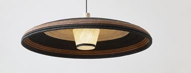 A close-up image of two pendant lights, each featuring a bell-shaped natural wood canopy from which a woven natural fiber shade hangs. The shades are multi-toned with alternating bands of light beige/natural and black woven material, creating a striped pattern. The wooden canopies exhibit a visible grain, and the black electrical cord is visible emerging from the top of the canopy. — 3D model