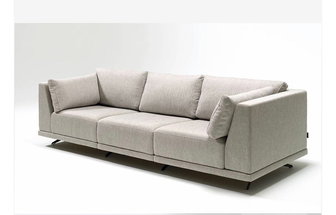 A three-seater modular sofa with a low profile and clean lines. It features plush seat and back cushions, with additional throw pillows. The sofa is upholstered in a textured, light grey fabric and rests on thin, dark metal legs that are set back from the main body, creating a floating appearance. The armrests are wide and integrated into the structure. — 3D model