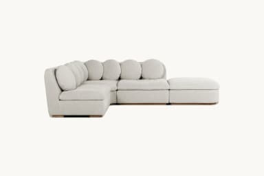 A modular sectional sofa with a chaise lounge. The sofa features a low profile with square seat cushions and rounded back cushions arranged in a series. It has a light-colored fabric upholstery and a visible wooden base. — 3D model