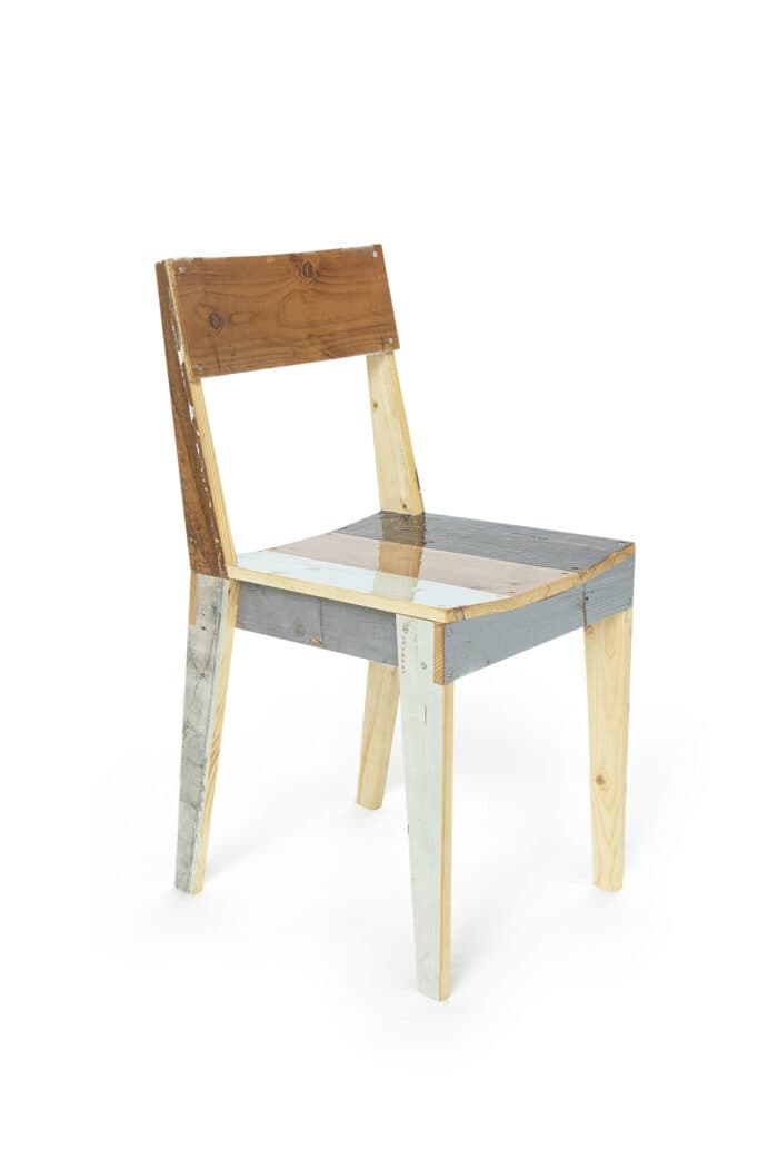 An armless side chair constructed from various pieces of reclaimed or repurposed wood, exhibiting a patchwork aesthetic. The chair features a rectangular backrest and a flat seat, with some wood pieces retaining a natural finish and others painted in distressed shades of grey, white, and light blue. It has a simple, straight-legged design with visible fasteners. — 3D model