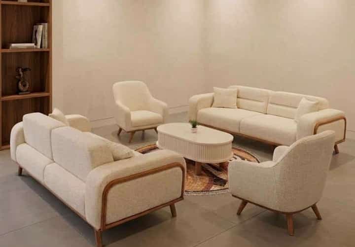 An oval-shaped modern coffee table featuring a white fluted body and natural wood splayed legs. — 3D model