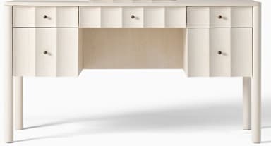 A light-colored, contemporary desk featuring a rectangular top with subtly rounded corners, supported by four tapered cylindrical legs. The desk includes multiple drawers, with the drawer fronts showcasing a distinct fluted or scalloped design, creating a textural element. Small, dark-toned spherical drawer pulls are present on each drawer. The overall aesthetic is clean and modern, with a focus on tactile surface detail. — 3D model
