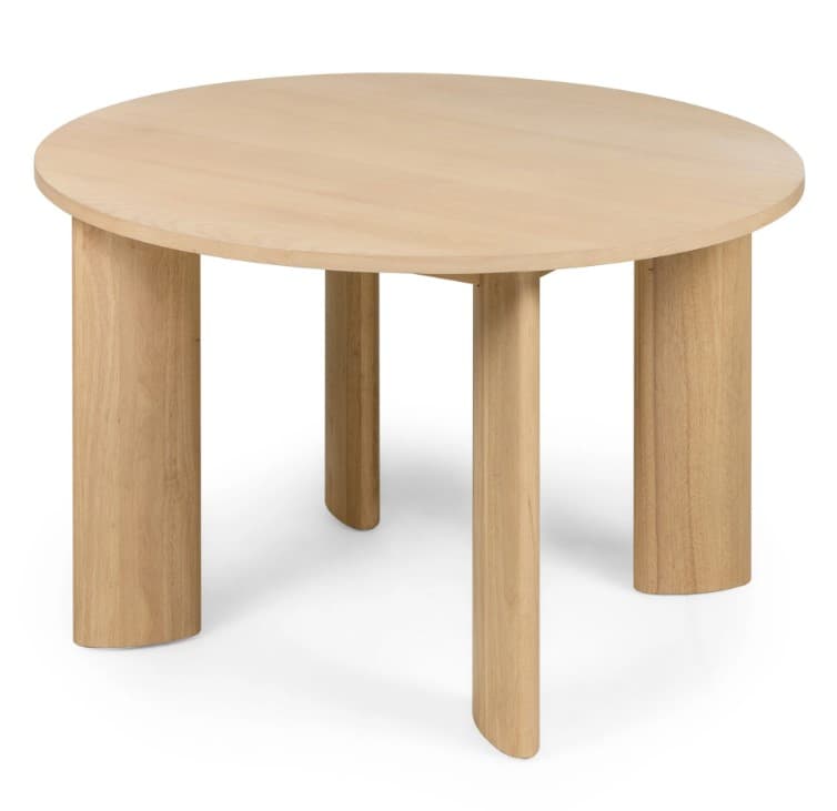 A round dining table crafted from light-toned wood, featuring a circular tabletop supported by four thick, sculptural legs. The legs have a unique curved profile, presenting a minimalist and contemporary aesthetic. The natural wood grain is visible throughout, indicating a solid wood construction or high-quality veneer. — 3D model