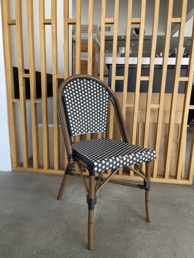 An armless chair with a curved backrest and straight legs, featuring a woven seat and back in a black and white checkerboard pattern. The frame is constructed from a dark wood-look material, likely synthetic rattan or wood. — 3D model