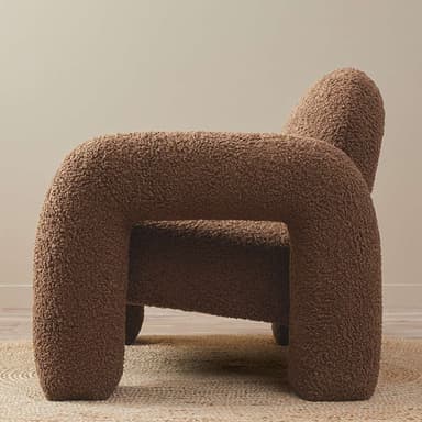 A modern armchair upholstered in a plush, textured teddy fabric. This chair features a rounded, enveloping silhouette with substantial, integrated armrests that flow seamlessly into the back and seat. Its thick cushioning and tactile surface invite comfort and relaxation. The overall design is contemporary, with clean lines and a soft, inviting appearance, supported by a sturdy, low-profile base. — 3D model