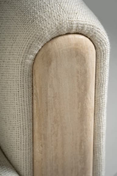 A large, curved sectional sofa upholstered in a light, textured boucle fabric, featuring a left-hand chaise extension and a unique right-hand armrest with a recessed wooden panel. The sofa includes several matching decorative pillows, both square and round. — 3D model