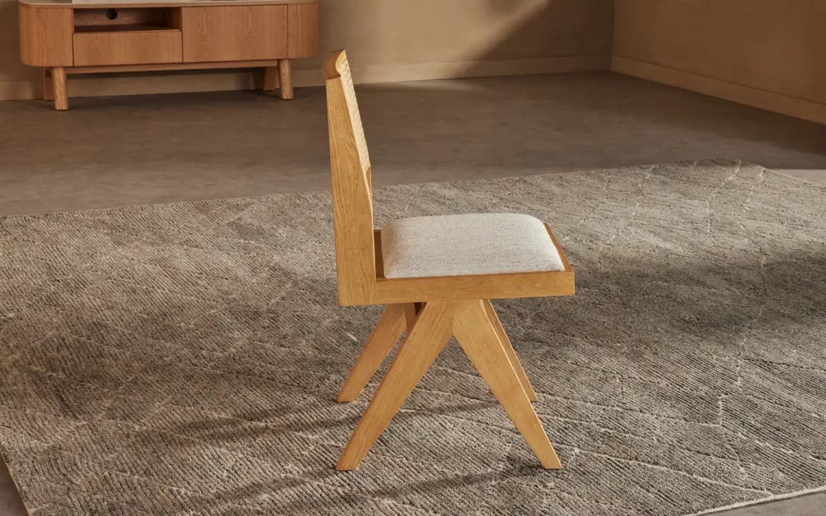 A modern dining chair with a minimalist design, featuring a wooden frame and a cushioned seat. The chair has a unique angular leg structure and a slightly reclined backrest. — 3D model