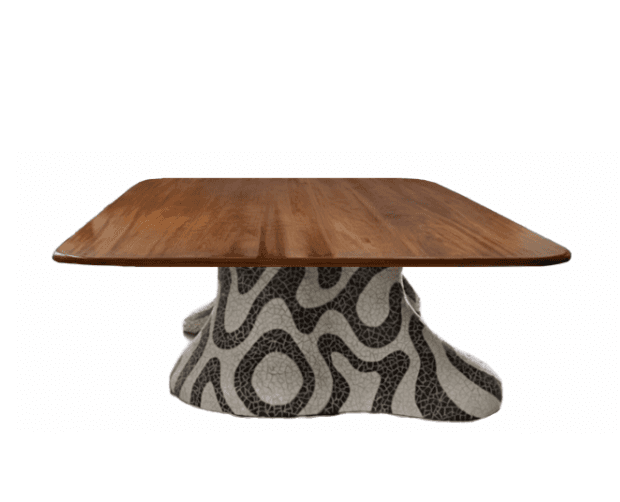 A low-profile coffee table with a distinct base. The tabletop is a rectangular slab with gently rounded corners, constructed from a warm-toned wood. The base is sculptural and appears to be made of a mosaic material, featuring an abstract, wavy pattern in black and white. The overall form suggests a modern or eclectic design aesthetic. — 3D model