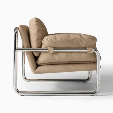 A modern armchair with a tubular chrome frame and plush, upholstered cushions in a camel or mustard yellow hue. The armchair features a low profile and a minimalist design, with the cushions appearing overstuffed and soft. The frame has a distinct cantilevered appearance. — 3D model