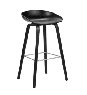 A modern black bar stool featuring a molded, ergonomically shaped seat atop four tapered wooden legs. A silver-colored square metal footrest connects the legs, providing support and stability. The overall design is sleek and minimalist. — 3D model