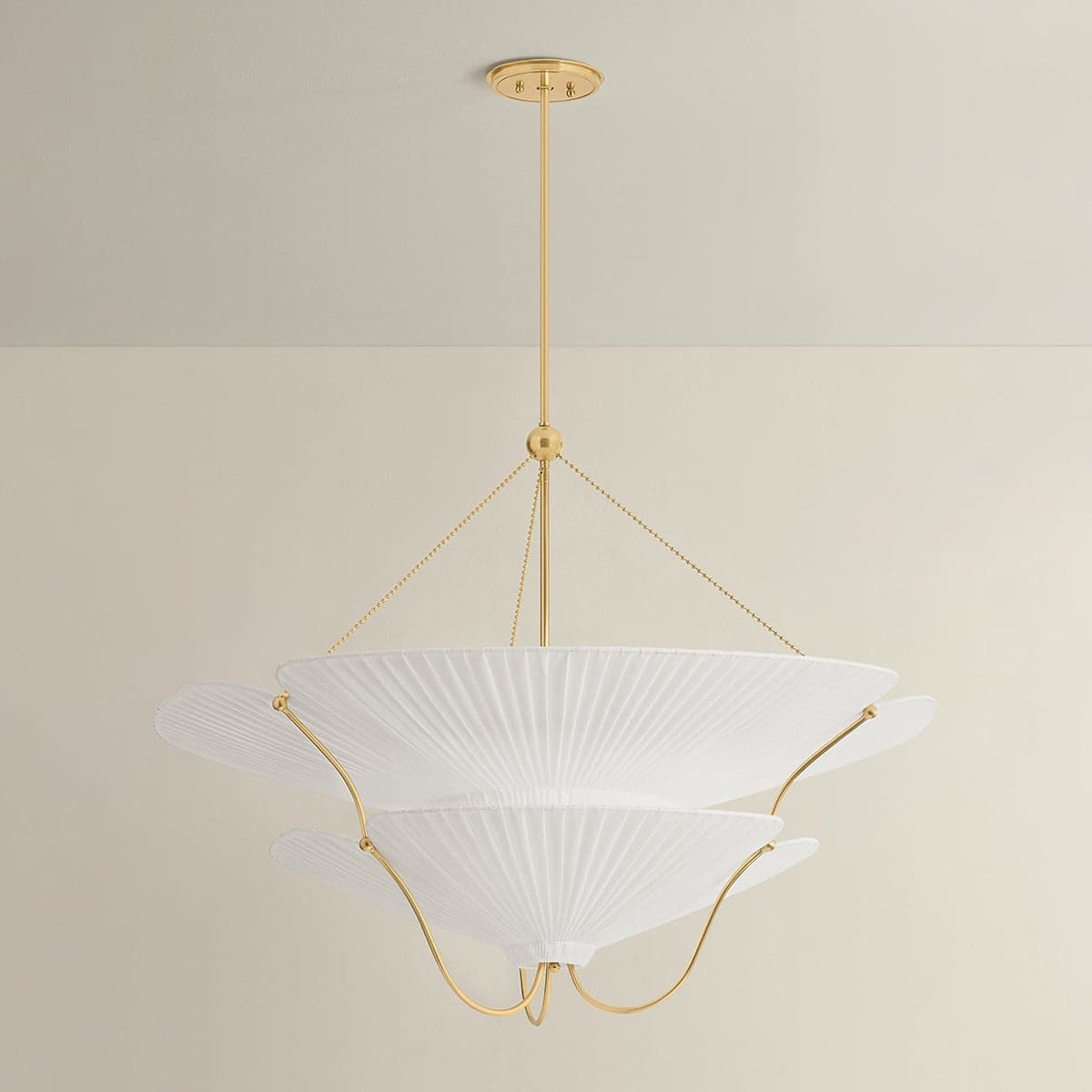 A contemporary tiered pendant light featuring multiple layers of white, finely pleated fabric shades suspended by a slender brass rod. The shades have a soft, scalloped edge design, and are supported by delicate brass chains and curved metallic rods. The light is designed to hang from a ceiling canopy, also finished in brass, providing diffused illumination through its layered textile structure. The overall aesthetic is elegant and modern. — 3D model