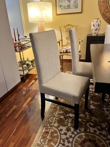 A contemporary upholstered dining chair featuring a light-colored, textured fabric covering both the seat and the tall backrest. The chair is supported by four straight, dark-stained wooden legs. Its design is armless, providing a clean and versatile profile. — 3D model