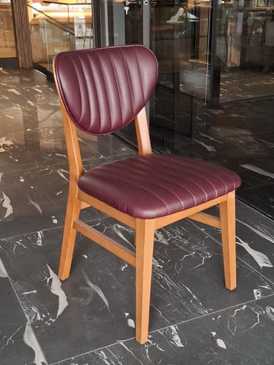 A modern dining chair constructed from a light brown wooden frame, featuring a distinctive rounded solid wood backrest and a channel-tufted upholstered seat in a reddish-brown (maroon) faux leather material. The chair's design emphasizes clean lines and a contemporary aesthetic, with the backrest appearing to be integrated seamlessly into the rear leg supports. — 3D model