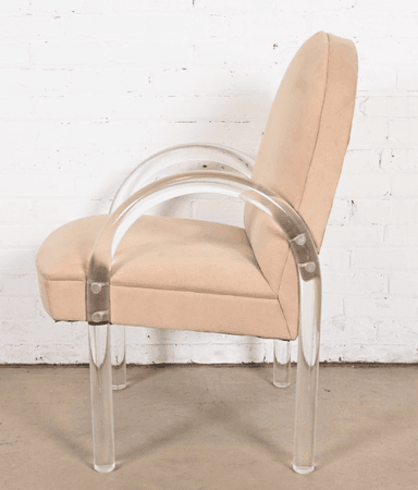 A contemporary armchair with a rounded back and upholstered seat and backrest. The chair features curved armrests and legs constructed from clear acrylic material. The upholstery appears to be a soft, textured fabric. The frame is supported by four cylindrical acrylic legs. — 3D model