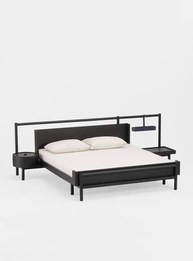 A modern dark wood bed frame with a headboard, accompanied by a cylindrical nightstand on one side and a larger, L-shaped bedside table on the other. The bed is made up with white bedding and pillows. A minimalist overhead structure extends from the headboard, supporting a dark blue hanging tray or basket. — 3D model