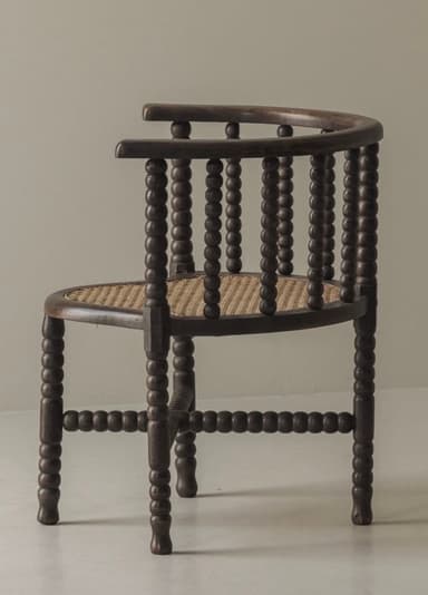 A dark stained wooden barrel armchair featuring a bobbin-turned frame and a woven cane seat. The back and armrests form a continuous curved structure, supported by vertical bobbin-turned spindles. The four bobbin-turned legs are connected by bobbin-turned stretchers forming an X-shape beneath the seat. The seat itself is crafted from woven cane with a slightly curved front. — 3D model