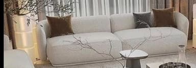 A contemporary modular sectional sofa in a light bouclé fabric, consisting of two low-profile units arranged in a chaise configuration. It features rounded edges and includes three accent pillows in brown and gray tones. — 3D model