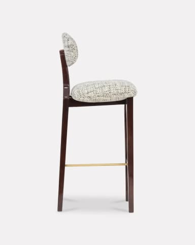A high-backed bar stool featuring a dark stained wooden frame, a contoured upholstered seat, and a separate, floating upholstered backrest. The frame includes splayed legs and a brass footrest. The upholstery is a textured, patterned fabric in monochrome tones. — 3D model