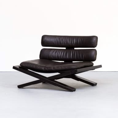 A modern low-profile lounge chair featuring a distinctive black X-frame base and rich brown leather upholstery. The seat cushion is a single, thick padded element, while the backrest is composed of two horizontal padded sections, providing support. The frame appears to be black-stained wood or matte black metal, creating a stark contrast with the warm brown of the cushions. The design emphasizes clean lines and a contemporary aesthetic. — 3D model