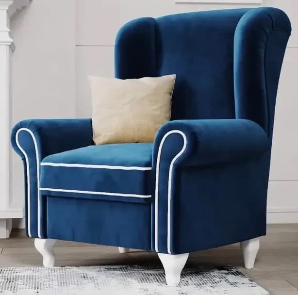 A classic wingback armchair upholstered in a rich, deep blue velvet fabric, featuring distinct white contrast piping along its edges, arms, and backrest. The chair has a high back with prominent wings, rolled arms, and stands on four short, subtly carved white legs, with the front legs exhibiting a gentle cabriole-like curve. A light beige throw pillow rests on the seat. — 3D model