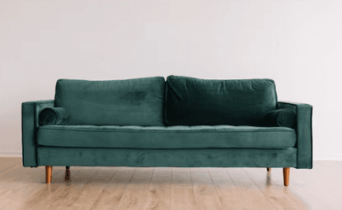 A modern two-seater sofa upholstered in luxurious emerald green velvet fabric, featuring button-tufted seat cushions, two rectangular back cushions, and narrow, straight armrests. It includes two matching cylindrical bolster pillows and stands on four light-colored wooden tapered legs. — 3D model