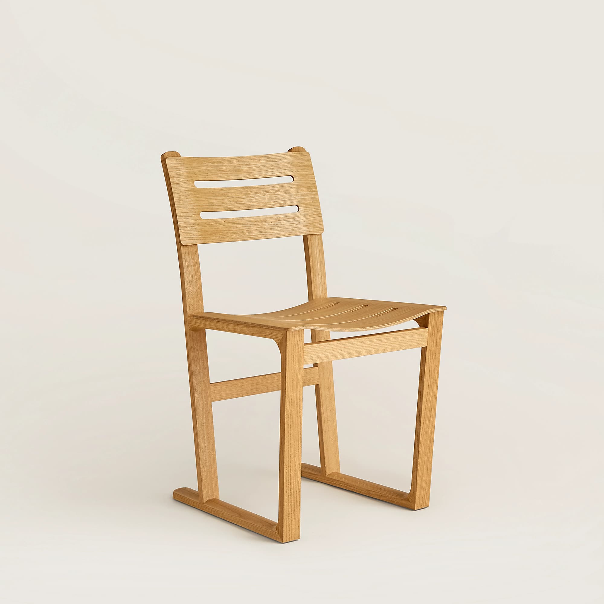 A modern wooden chair with a slatted seat and backrest. The chair features a minimalist design with clean lines and a light wood finish. The backrest has two horizontal slatted openings. The seat is also comprised of curved slats. The legs are straight and form a continuous base structure. The overall construction suggests a focus on both aesthetics and functionality. — 3D model