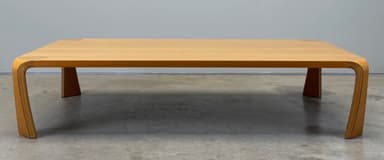 A modern rectangular coffee table constructed from molded plywood with a light wood veneer finish. It features a seamless design where the tabletop curves down to form the legs, complemented by two discrete dark central supports. — 3D model