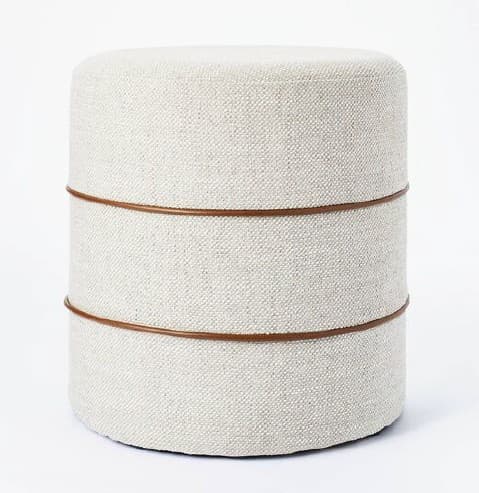 A contemporary cylindrical ottoman featuring off-white textured fabric upholstery and two thin, dark brown decorative bands encircling its body. — 3D model