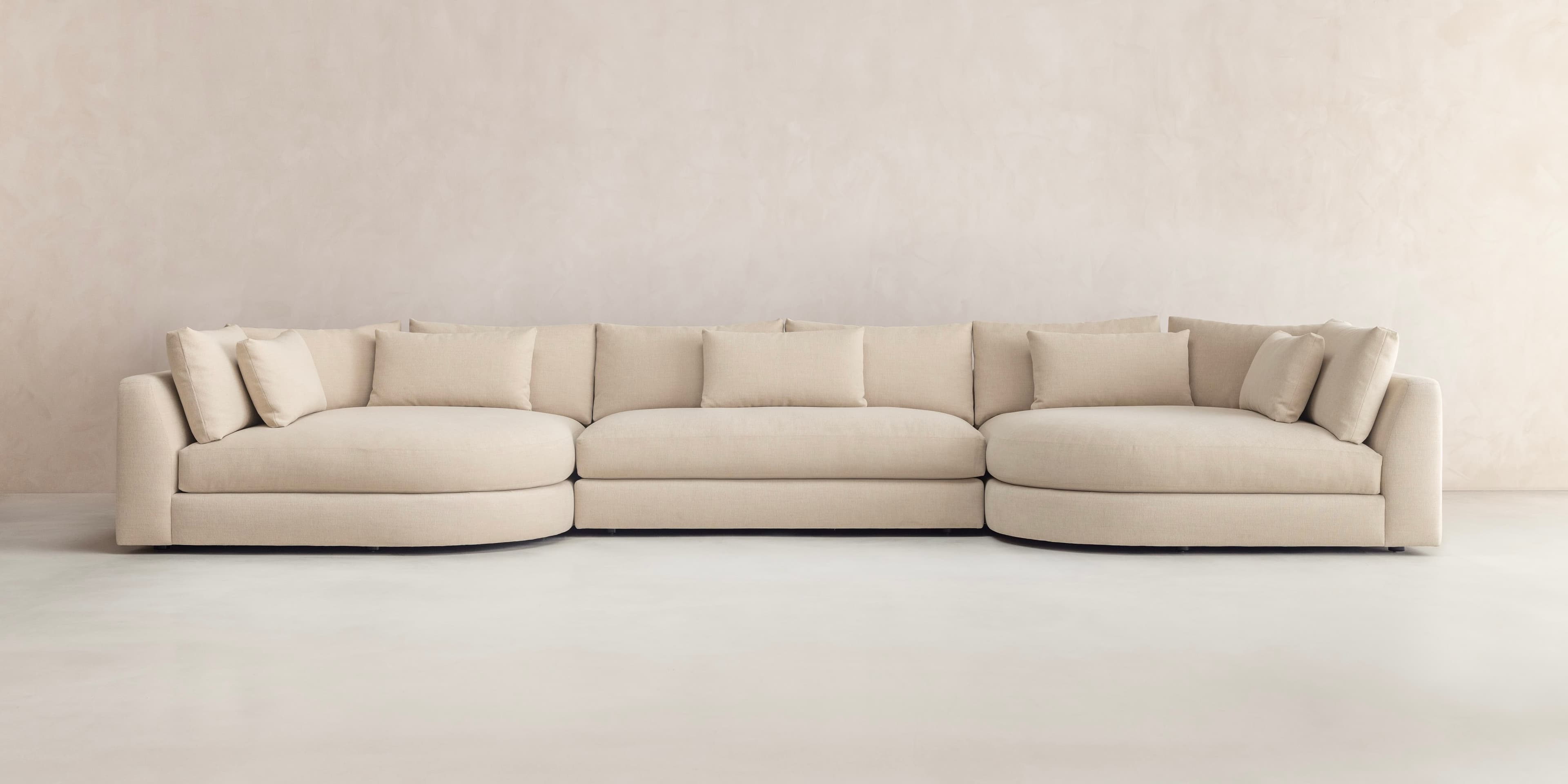 A large, U-shaped modular sectional sofa upholstered in light beige fabric, featuring various straight and curved sections, loose back cushions, and wide track arms, designed for extensive seating. — 3D model