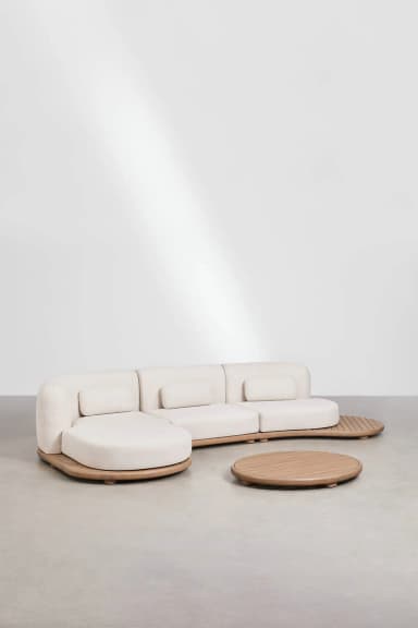 A modular sectional sofa with a curved chaise lounge on one end. The sofa features a light-colored upholstered body and loose back cushions. The base and accents are made of light-colored wood, with a slatted design on the extended side panel. A circular, low-profile coffee table with a slatted wooden top is positioned in front of the sofa. — 3D model