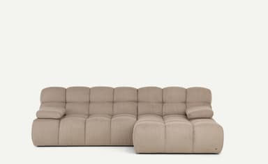 A light beige, modular sectional sofa featuring a chaise lounge component on the right side. The entire sofa is upholstered in a ribbed corduroy fabric, giving it a plush, textured appearance. It consists of deep, blocky cushions for both the seat and backrest, arranged in a low-profile, contemporary style. The armrests are similarly upholstered and integrated, providing a soft, rounded look. — 3D model