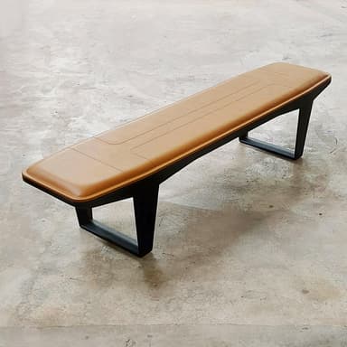 A long, rectangular bench featuring a padded, tan upholstered seat with stitched detailing, supported by a minimalist black metal frame with inverted V-shaped legs. — 3D model