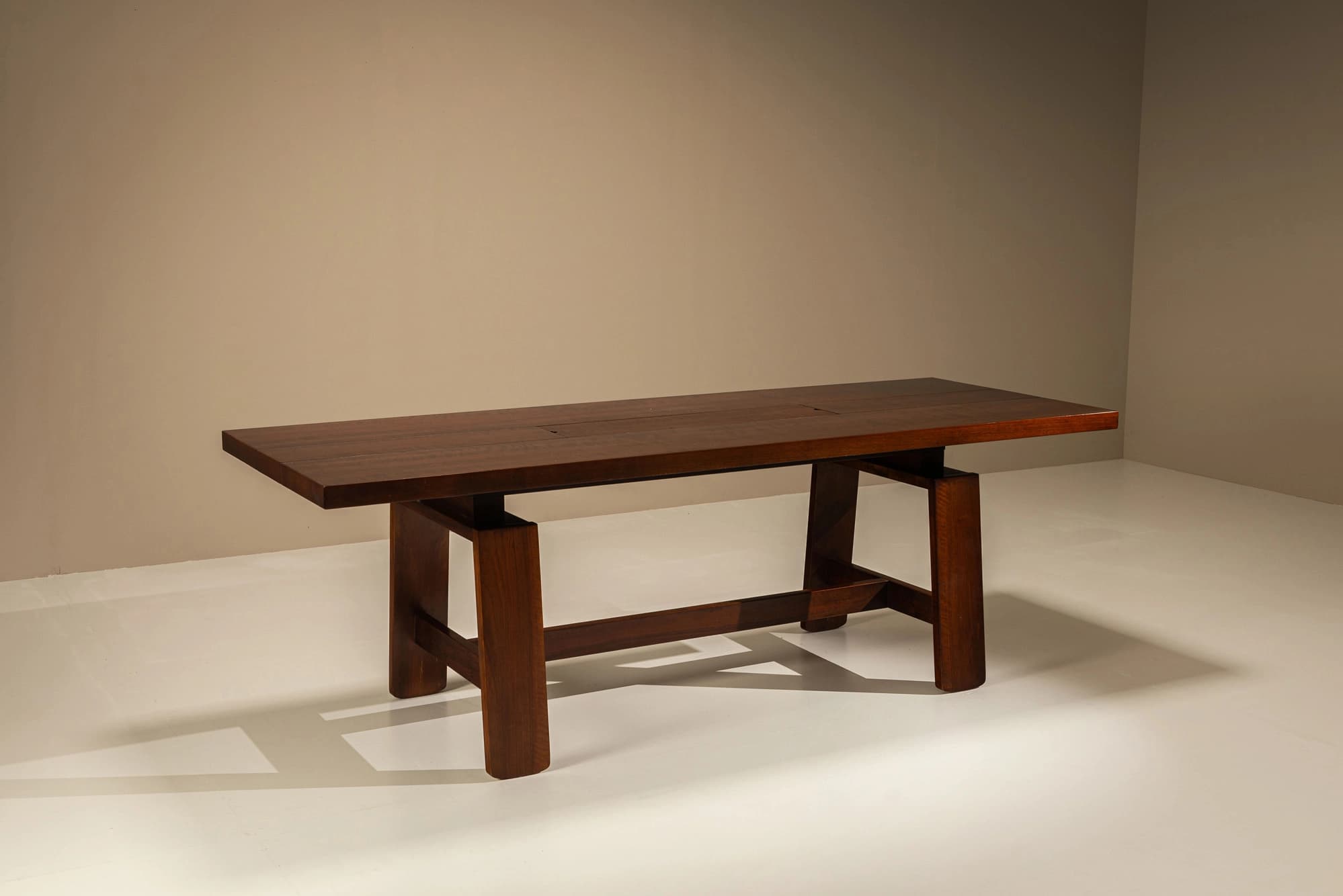 A large, rectangular solid wood table featuring a robust trestle base and a planked top. The top surface incorporates two flush-mounted rectangular covers, possibly for integrated power or cable management. The wood has a dark, rich finish. — 3D model