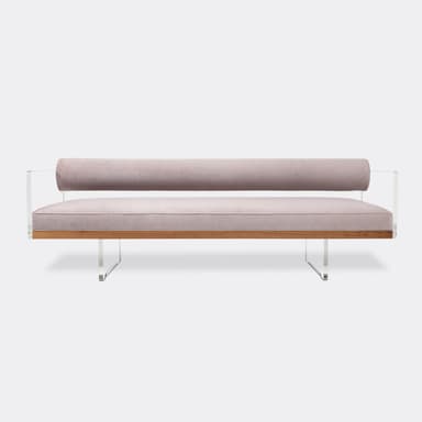 A sleek, modern daybed featuring a rectangular seat cushion and a cylindrical bolster backrest, both upholstered in a soft, light pink velvet. The seating elements rest on a visible walnut wood base, which is supported by transparent acrylic (Lucite) side panels that also hold the bolster cushion in place. Exposed circular fasteners with a polished finish are visible along the side of the wooden base. — 3D model