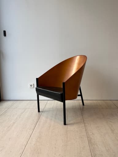 A striking mid-century modern lounge chair featuring a gracefully curved, light-brown plywood shell that forms both the backrest and integrated armrests. The chair is supported by a minimalist black metal frame with slender legs. A dark, possibly black or dark brown, upholstered cushion rests on the seat, contrasting with the warm wood tones. — 3D model