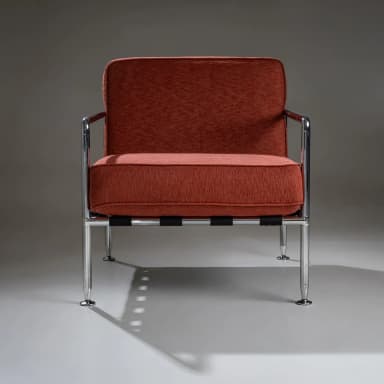 A pair of armchairs with a modern design. Each chair features a polished chrome frame, including the armrests and legs. The seating and back cushions are upholstered in a textured, rust-colored fabric. The seat support appears to be constructed from woven straps. The chairs have a minimalist aesthetic, emphasizing clean lines and industrial materials. — 3D model