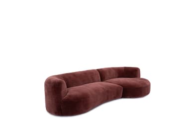 A large, contemporary curved sofa upholstered in a rich, burnt orange velvet or similar plush fabric. The sofa features a continuous, undulating form with a low backrest and seamlessly integrated armrests. Its design is characterized by soft, rounded edges and a low-profile base, giving it a sleek and inviting appearance. Decorative pillows and a vase with dried botanicals are placed on one end of the sofa. — 3D model