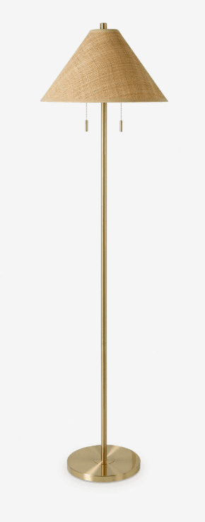 A modern floor lamp featuring a slender brass-finished metal body and a conical lampshade made from woven jute or rattan. The lamp has a circular base and includes two pull chains for operation. — 3D model