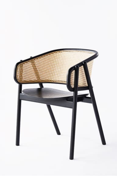A modern armchair featuring a black finished solid wood frame, a natural cane woven backrest, and a light grey upholstered seat cushion. The chair has a sleek, minimalist design with integrated armrests that flow from the backrest. — 3D model