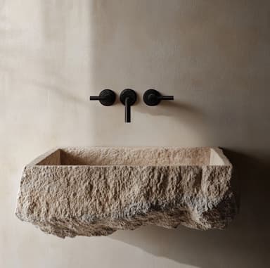 A rectangular stone vessel sink with a rough, natural exterior and a smooth interior. It features a black wall-mounted faucet with two handles and a spout, and a black drain cover within the basin. — 3D model