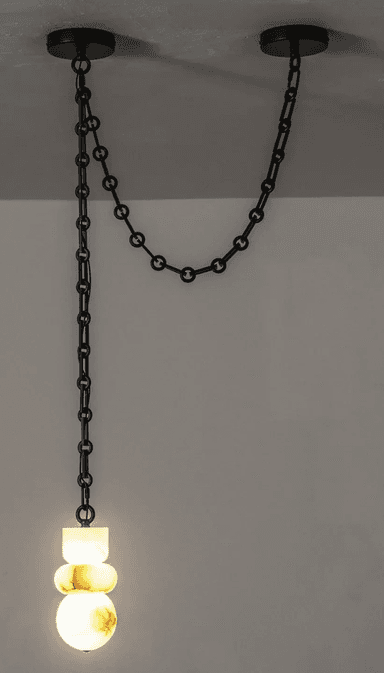 A contemporary pendant light featuring a sculptural shade crafted from translucent alabaster, suspended by a black metal chain system. The shade is composed of three stacked, organic, rounded forms, illuminated from within to highlight the natural veining and luminous quality of the stone. The suspension system consists of a long chain dropping from one ceiling mount, connecting to the light fixture, and a shorter chain extending horizontally to a second ceiling mount, creating a distinctive draped effect. — 3D model