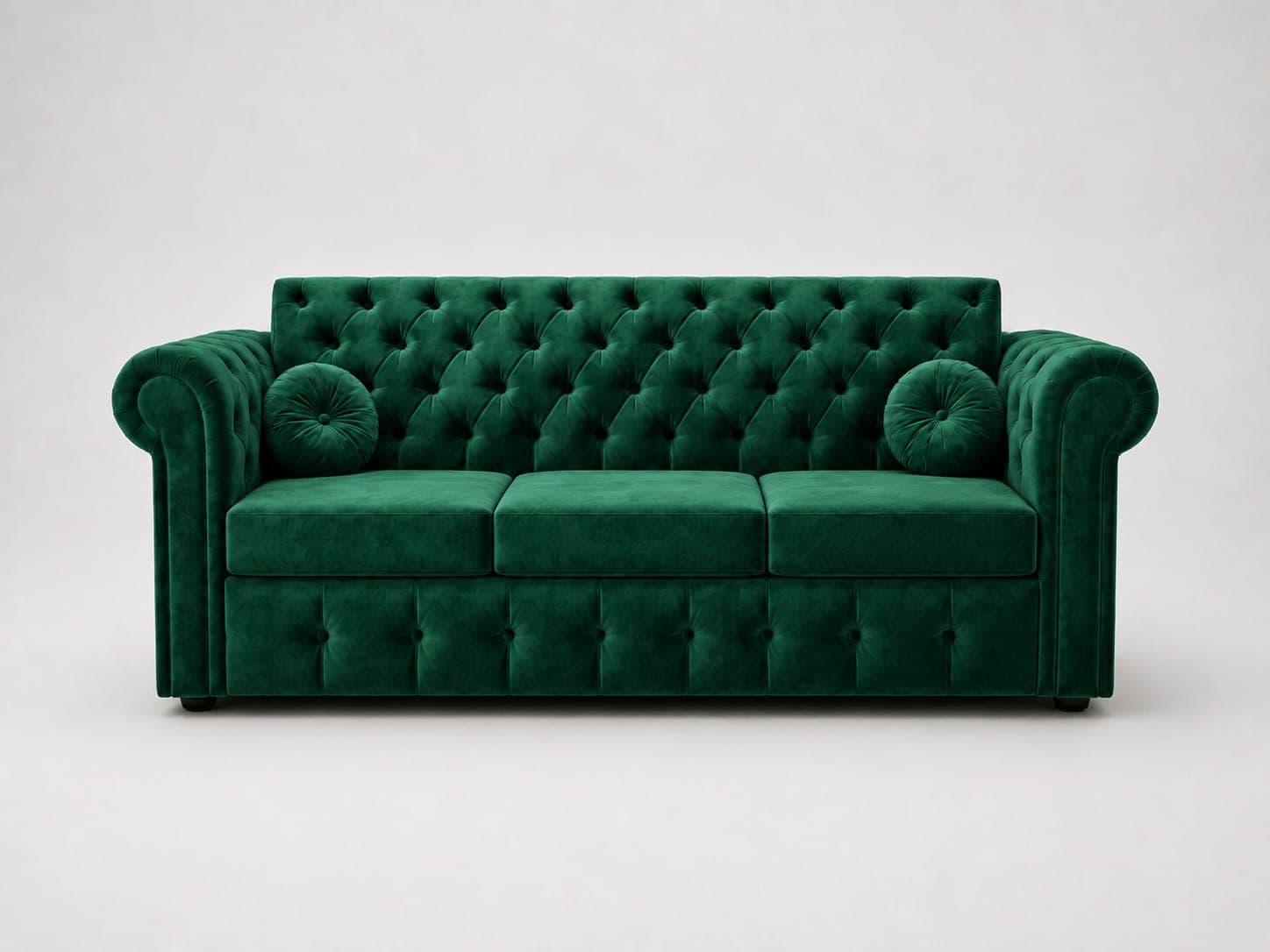 A luxurious emerald green velvet Chesterfield sofa with deep button tufting on the backrest, rolled arms, and front apron. It features three distinct seat cushions and comes with two round bolster pillows, upholstered in matching velvet. The sofa exhibits a classic and elegant aesthetic, appearing in pristine condition. — 3D model