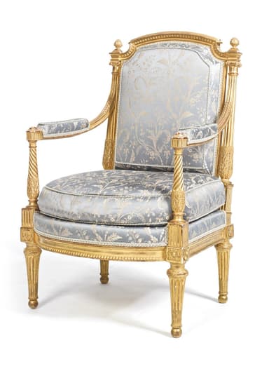 An ornate Louis XVI style armchair featuring an extensively gilded and carved wooden frame, upholstered in a light blue-gray brocade fabric with a gold floral pattern. It has a high, rounded back, padded armrests, fluted tapered legs, and decorative finials. — 3D model