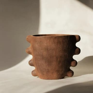 A rustic, short terracotta planter with a distinctive ribbed exterior, featuring an organic, hand-molded appearance. The unglazed surface has a textured, earthy finish, and the opening is wide and circular. The base is slightly narrower than the top, and the pronounced, rounded ribs wrap around the body of the vessel, giving it a unique, sculptural quality. — 3D model