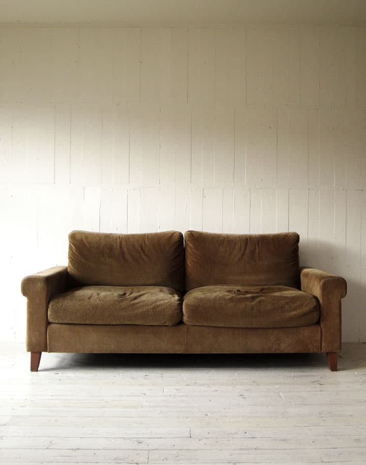 A two-seater sofa with a brown textured upholstery. The sofa features rolled arms, plush seat and back cushions, and short wooden legs. The design appears to be contemporary with a classic silhouette. The upholstery has a fine corduroy-like texture. — 3D model