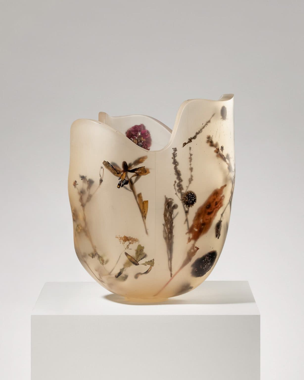 An irregular, organic-shaped vase crafted from translucent resin with various dried botanicals, including leaves, flowers, and stems, embedded within its walls. The resin exhibits a yellowish-amber hue and a matte, frosted finish. The top rim is uneven and undulating, contributing to its sculptural quality. — 3D model
