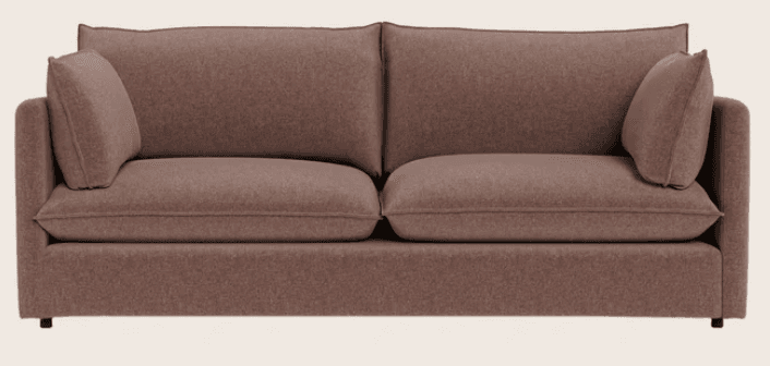 A contemporary three-seater sofa with a muted rose or dusty pink fabric upholstery. It features clean lines, wide track arms, two deep seat cushions, and multiple loose back cushions with piped edges, suggesting a comfortable and casual design. The sofa has a low profile with minimal or hidden feet. — 3D model